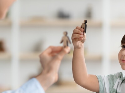 A child and counselor use wooden figures during a play therapy session.