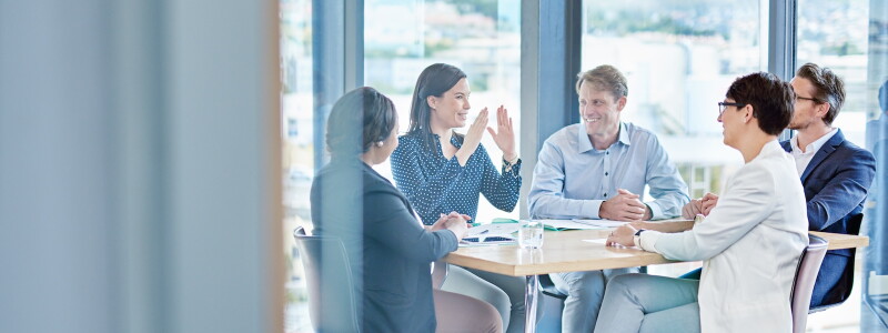 Colleagues enjoy a collaborative meeting around a table in front of large windows