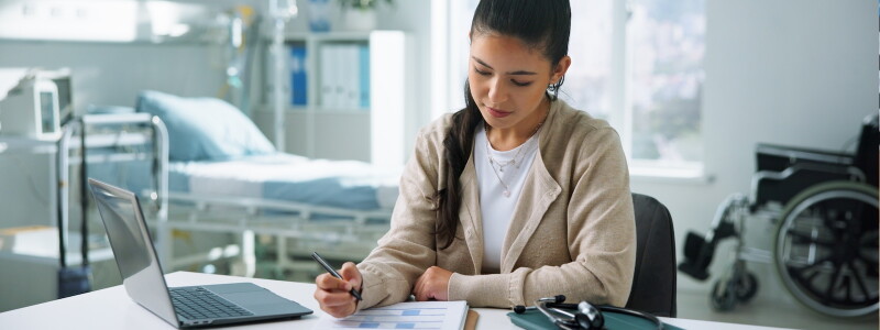 A nurse case manager sits in a hospital room working on paperwork.