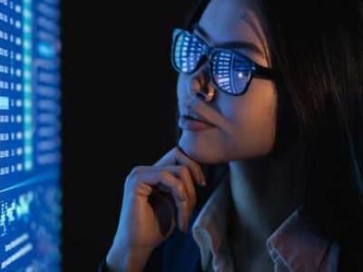 woman with glasses looking at blue screen full of data