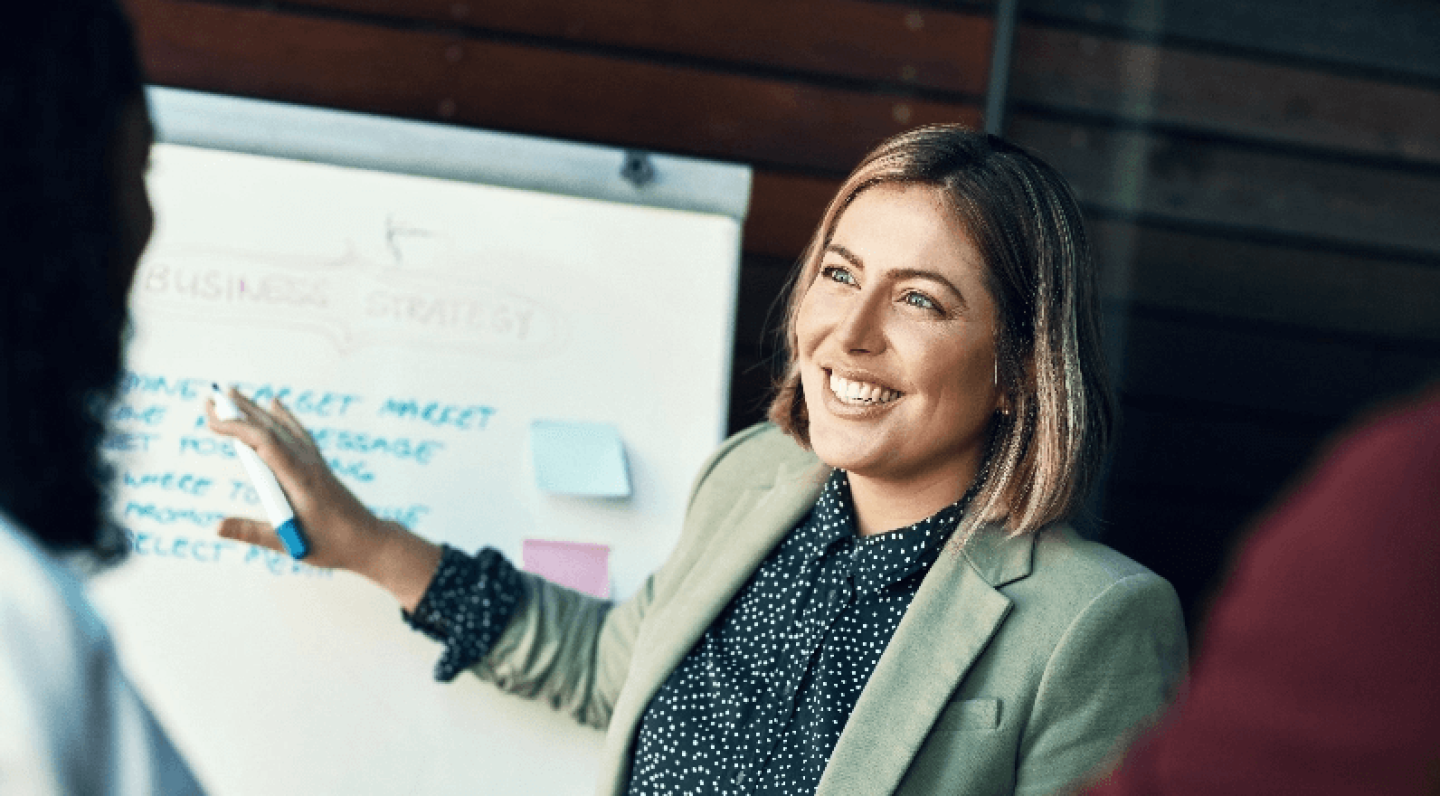 Smiling woman in blazer pointing at content on a whiteboard