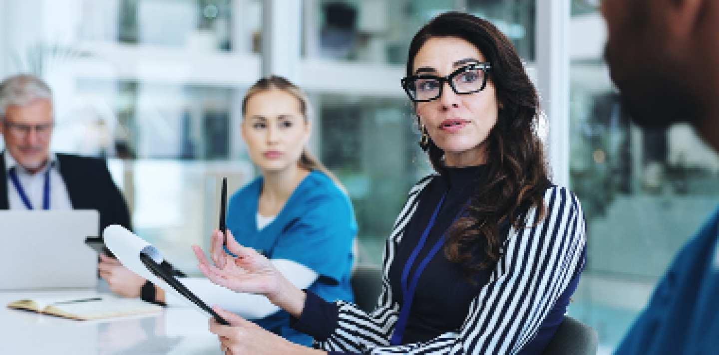 woman with glasses looking at a table with her team looking at someone speaking