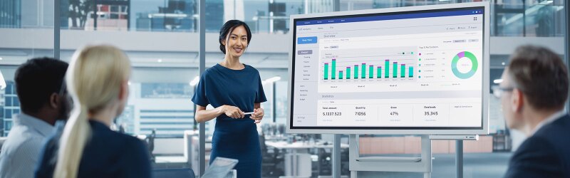 A business professional presents data insights on a large screen to a team.
