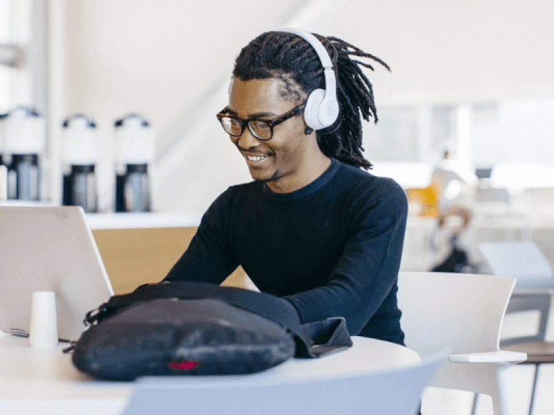 Man seated in coffee shop working on laptop wearing headphones