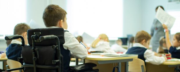 Student in a wheelchair sits at a desk in a classroom.