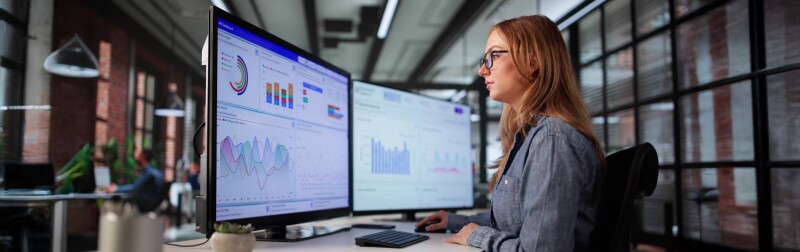 A young female data scientist analyzing financial data on computer screens.