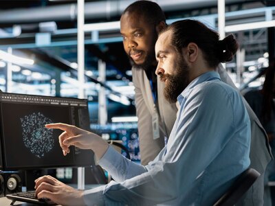 two men looking at double monitors displaying AI images