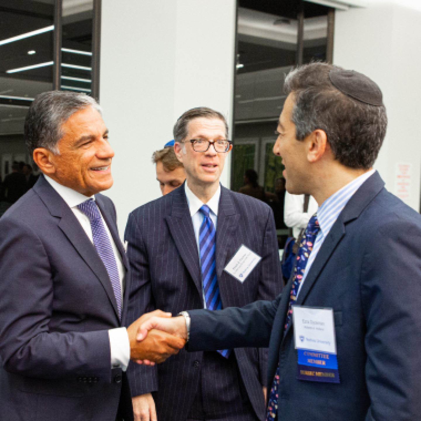 A group of male real estate colleagues shake hands at an event.