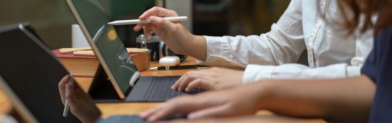 Two female workers consulting on their project while working with mock-up tablet on wooden table.