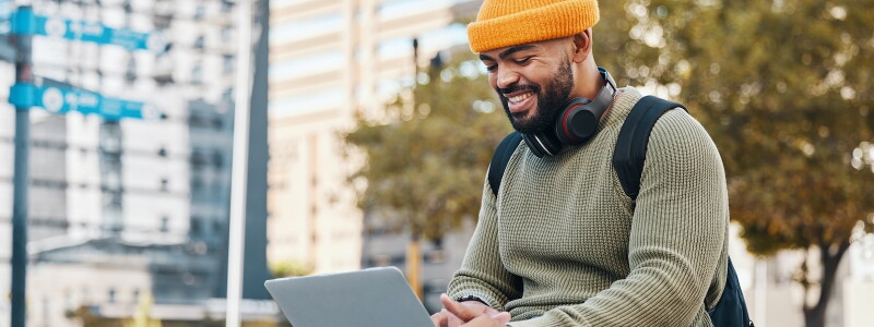 A man works remotely on a scholarship application on his laptop in the middle of the city.
