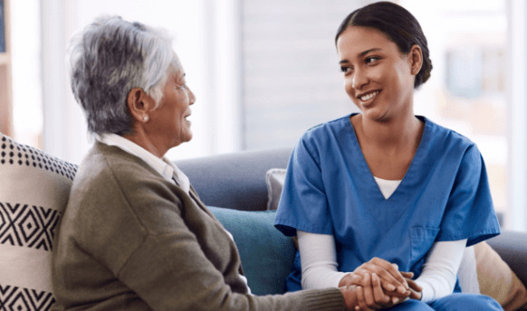 Nurse in uniform seated on couch and holding hands with older patient