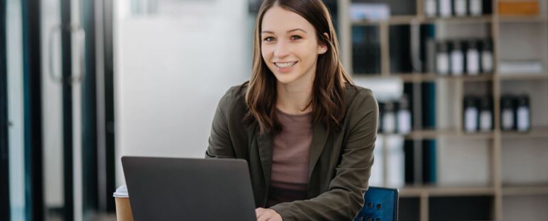 Woman seated in office working on laptop in front of shelf of books