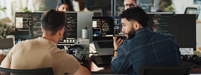 Two male workers sit in front of computers in an open office.