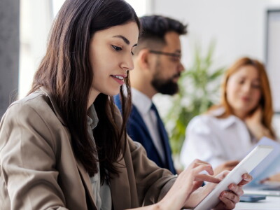 Side view of focused female employee scrolling on tablet while sitting in an office with coworkers.