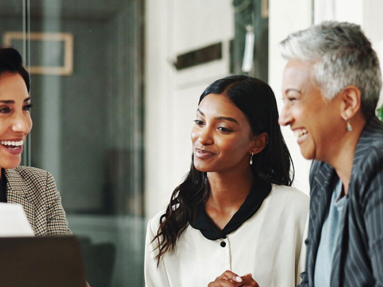 Business professionals are engaging in a collaborative and cheerful discussion in the office, highlighting communication and leadership skills developed through an MBA program.
