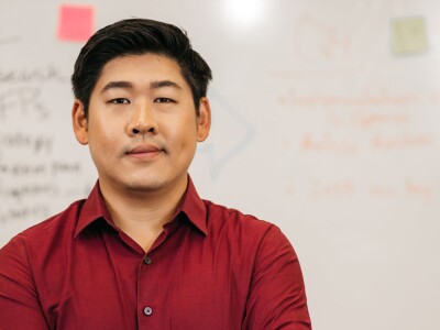 Asian man standing in front of a whiteboard with writing and sticky notes.