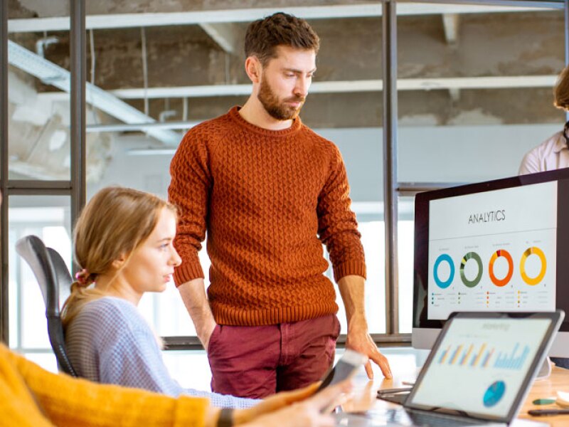 Group of young coworkers dressed casually working together on the computers with some charts sitting in the modern office interior.