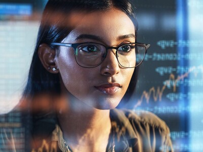 A woman analyzing data on a screen, with reflections of digital information overlaid on her glasses