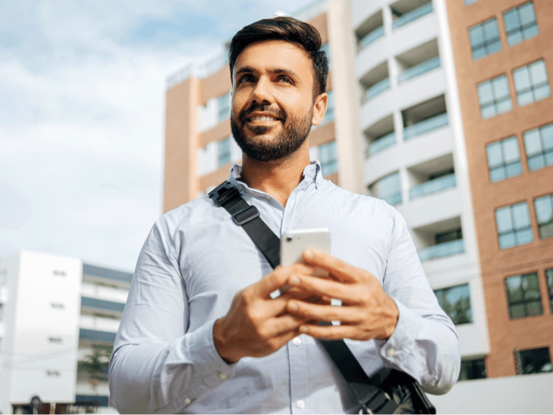 Man with shoulder bag outside holding cell phone