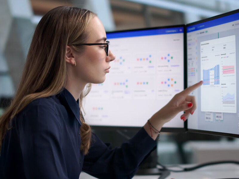 Young female marketer designs personalized email campaigns on three large computer screens.