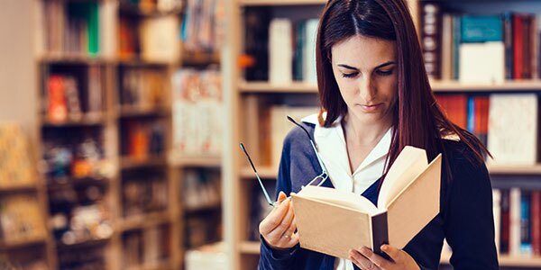 woman standing reading book and holding glasses