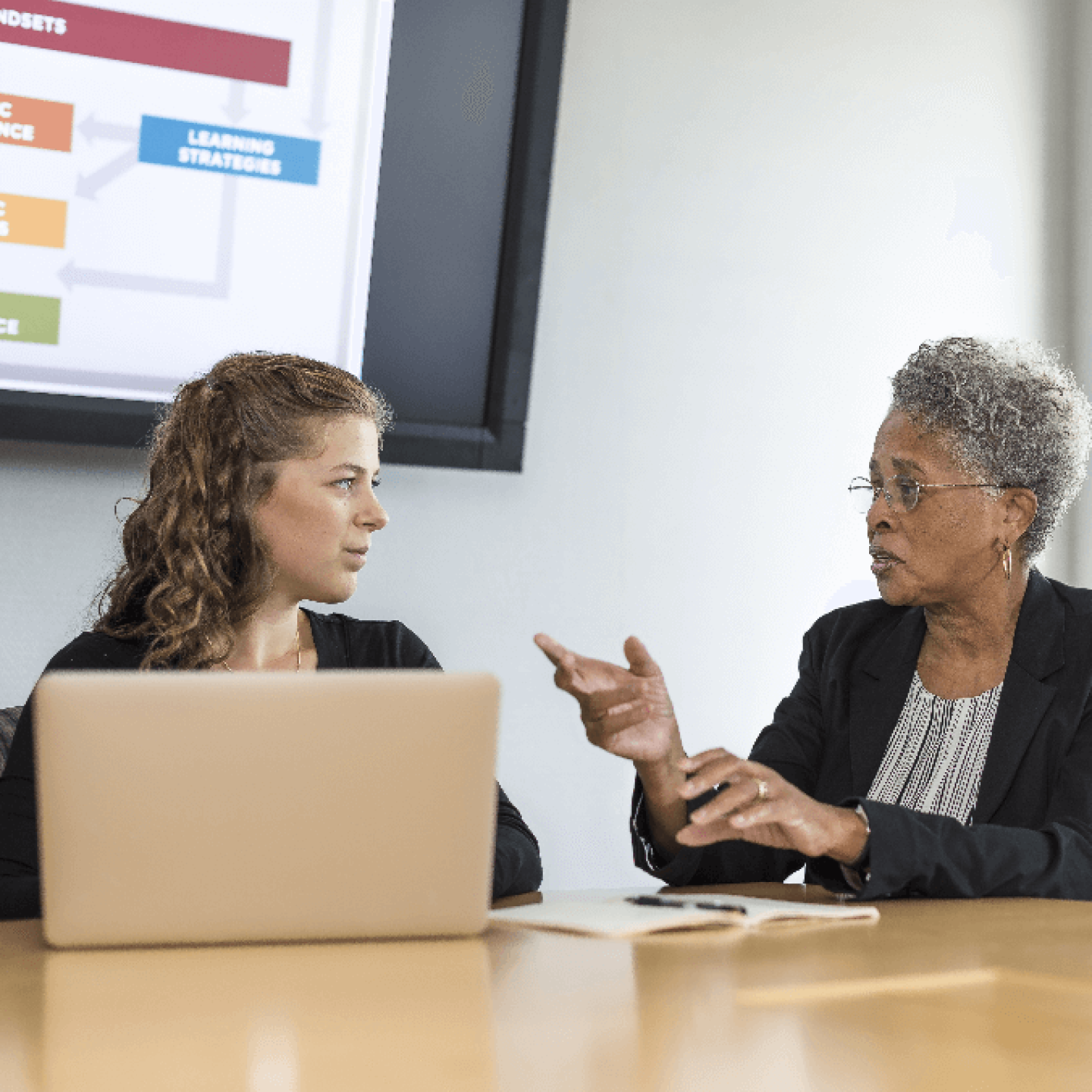 Two women seated at conference table talking
