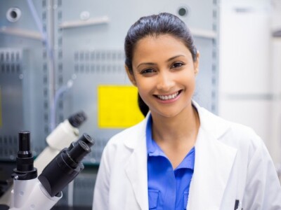 woman looking straight ahead smiling next to a microscope