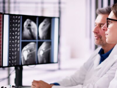 Two doctors are reviewing scans and consulting a patient via video call.