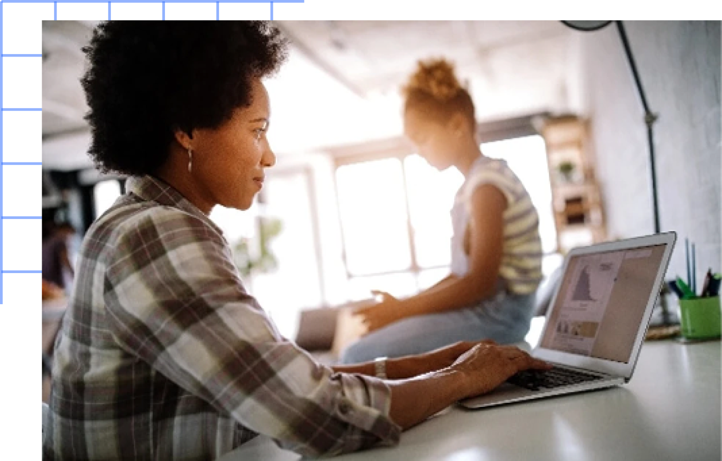 Young black woman works on laptop while female child sits next to her.