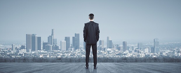 Man in a business suit stands with his back to the camera, staring at the city skyline