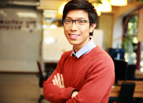 Man in sweater stands confidently with arms folded in office