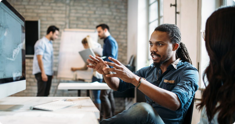 Team collaborating in a modern office, with one person explaining ideas and others working in the background.