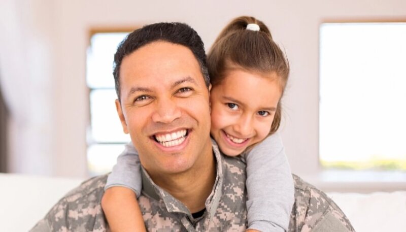 Man in army uniform with daughter on shoulders