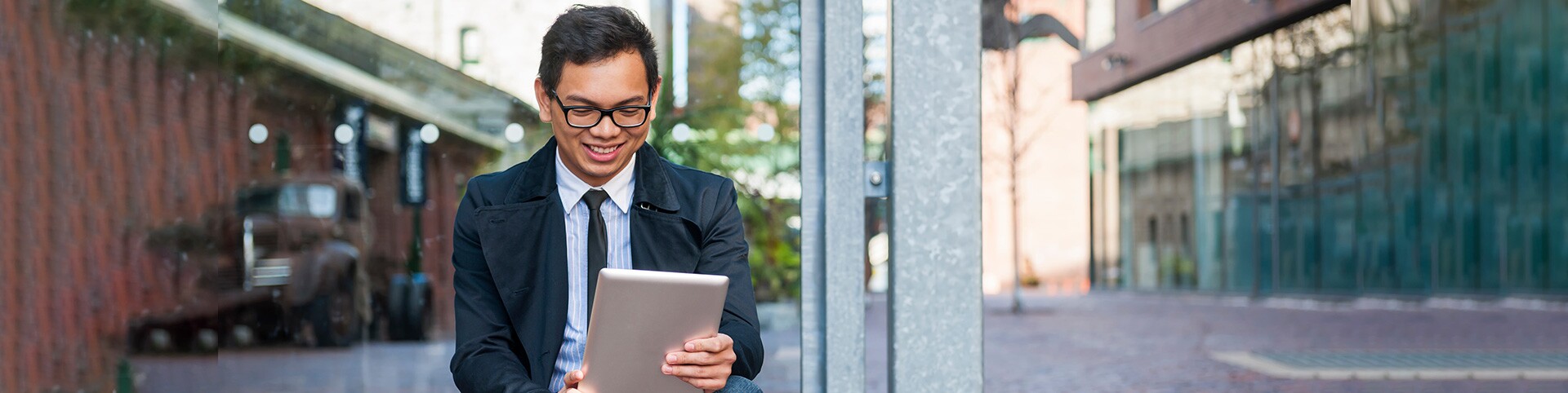 Man in dress clothes outdoors looking at tablet