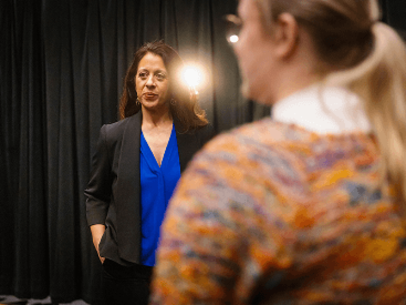 Woman in front of spotlight speaking to woman with orange shirt
