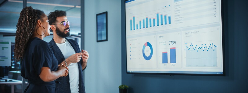 Two marketing professionals, a man and a woman, examine data projected on a screen.