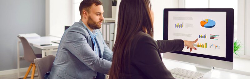 Two businesspeople analyzing data charts while looking at financial metrics on computer screen.