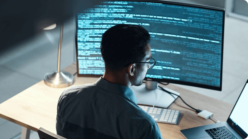 Engineering manager seated at desk working at desktop and laptop computer