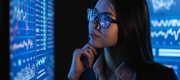woman with glasses looking at blue screen full of data