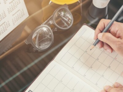 person writing in planner with calendar and glasses in front of them