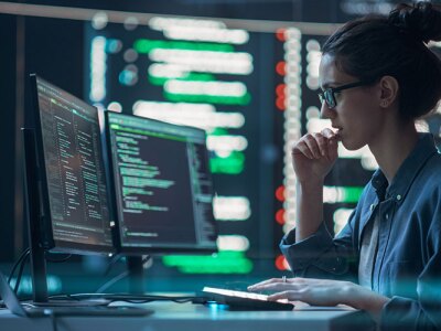 A woman looking at code on a computer monitor.