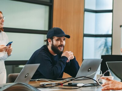 A person is leading a discussion at a whiteboard with sticky notes, while others participate in conversation