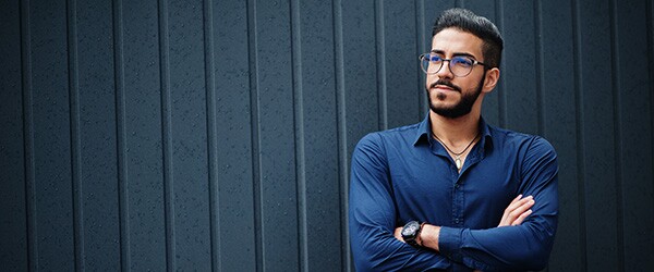 Bearded man in glasses and a blue shirt stands with his arms folded across his chest