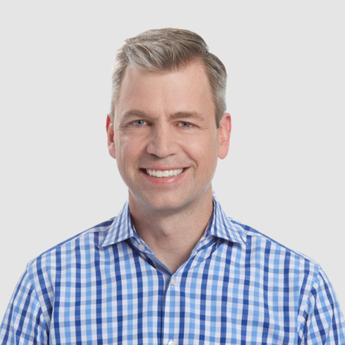 Headshot of a smiling man with short gray hair wearing a blue checkered shirt against a light gray background.