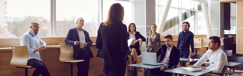 Various businessmen listen to female business leader during corporate meeting.