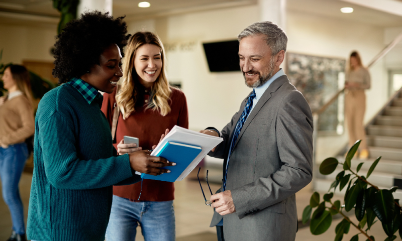 3 smiling colleagues gathered in a circle, reviewing shared material
