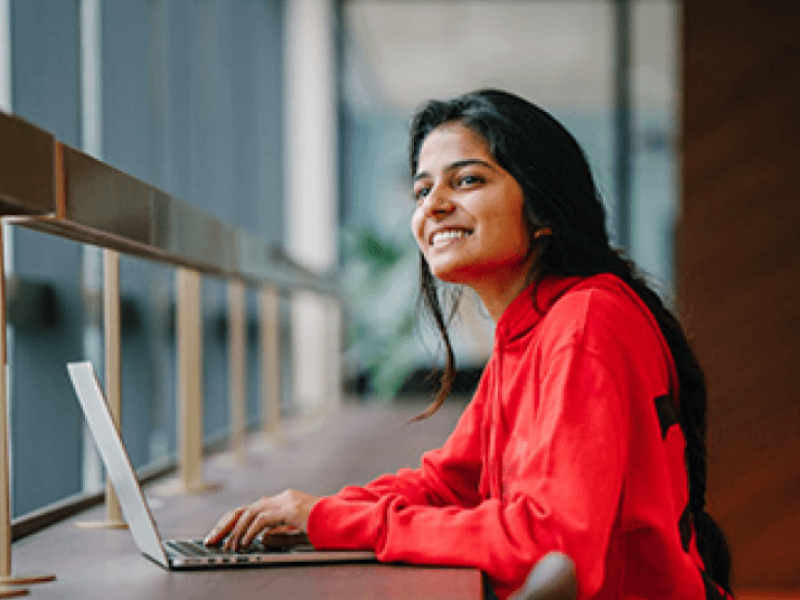 Woman smiling in red shirt using laptop