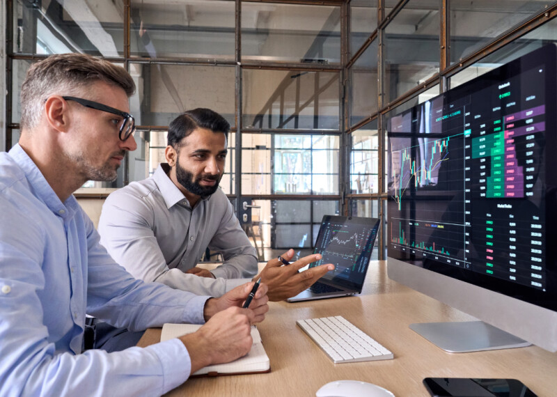 Two men seated at a desk reviewing data on a large computer monitor