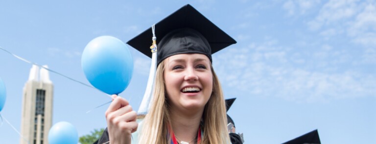 Graduate in cap and gown holding blue balloons