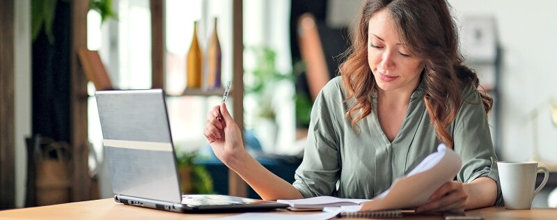 Woman in home office looking at papers and laptop